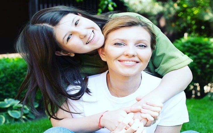 Aleksandra Zelenskaya in a light green dress hugging her mother in a white t-shirt and blue jeans.